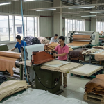 Realistic footwear cutting department scene, clicker cutting leather using patterns