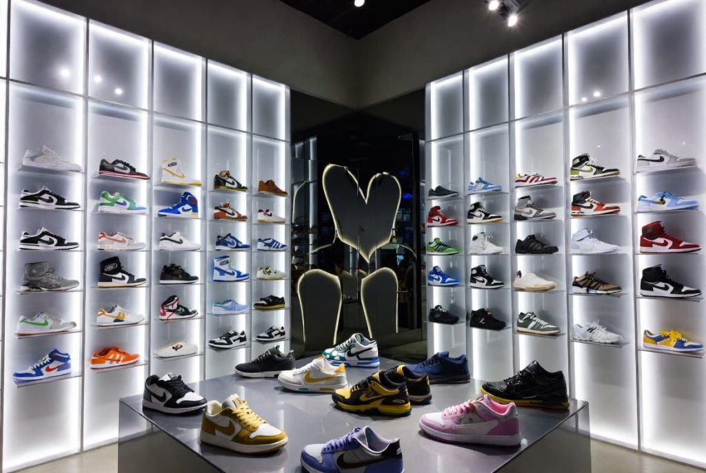 A luxury multi-brand sneaker display wall inside a bright, modern footwear store location.
