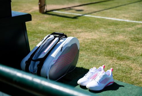 Luxury performance athletic tennis shoes with vibrant pink design accents sitting on a premium grass-court tournament sideline.