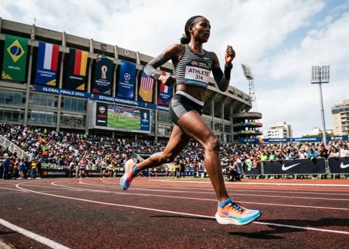 Low-angle shot of a runner sprinting with a sports stadium in the background.