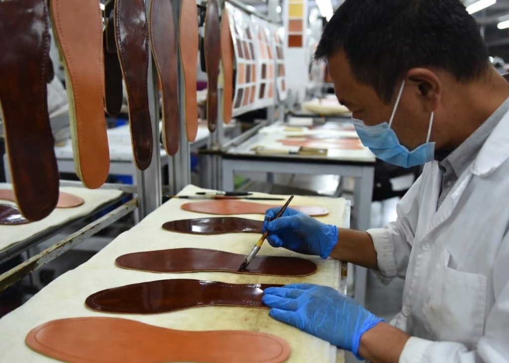 Technician performing bottom coloring on premium leather outsoles inside a footwear manufacturing factory.